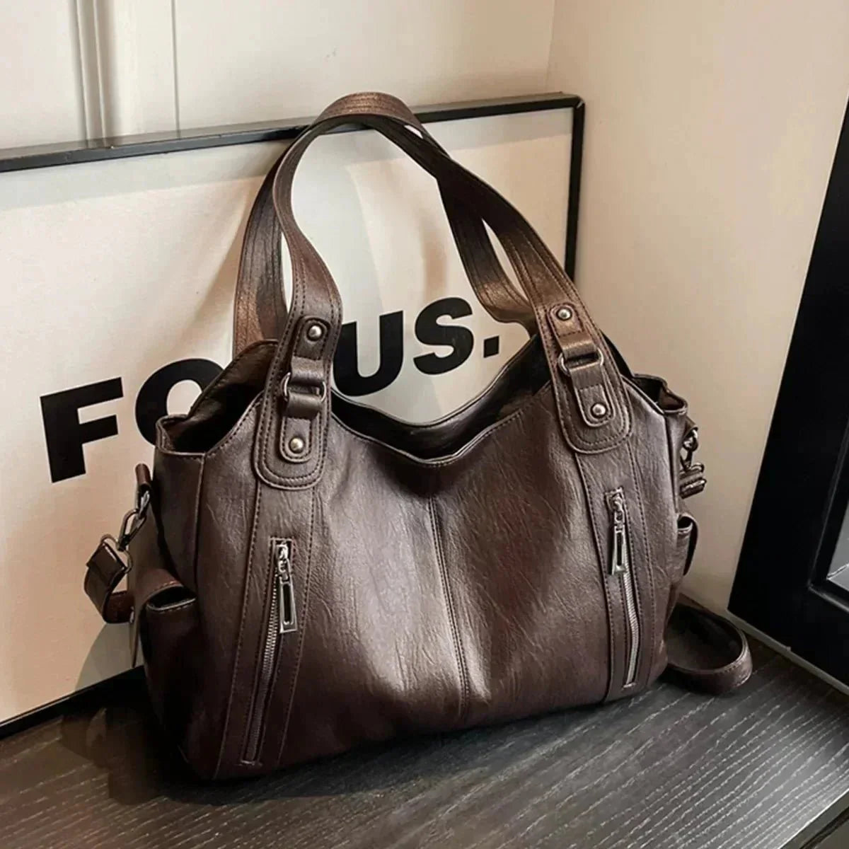 Dark brown stylish women's shoulder bag with zipper pockets on a tabletop